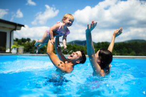 Young family with small daughter in swimming pool outdoors in backyard garden, playing